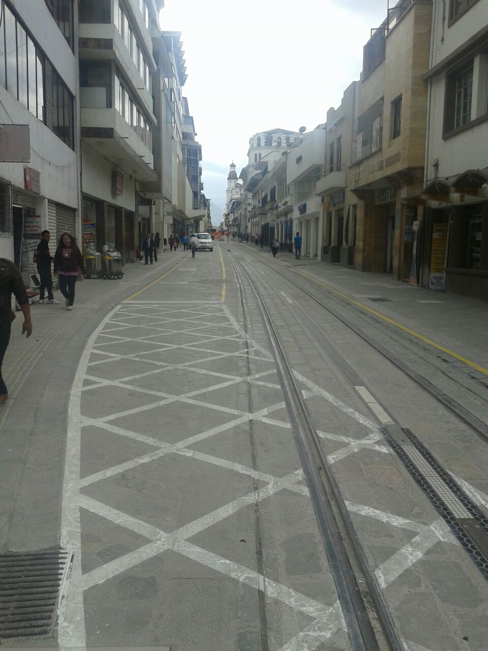 Žluté lineární pruhy jasně limitují akční rádius silničních vozidel, bílé překřížené poté určují, kterými místy se smí přejíždět drážní těleso. Přístup automobilů do na snímku vyobrazené ulice Gran Colombia nebyl zcela vyloučen, aby nebyli poškozeni místní rezidenti a obchodníci, některá odbočení, zejména ta potenciálně nejrizikovější, ovšem byla nově vyloučena, čímž se má nejen zvýšit bezpečnosti, ale i zamezit zbytečným prostojům tramvaje v ulicích. Drážní těleso není v centru Cuency záměrně od ostatního provozu odděleno jinak než vizuálně či drobnými prvky, tak aby se mohlo přirozeně zakomponovat do koloritu města. Chodci jsou vyzýváni k využívání chodníků, ve svobodném přechodu ulice jim ovšem nebude bráněno. Tím se vytvoří zóna, která dává všem vlastní prostor a zároveň nikoho výrazněji neomezuje. (foto: Tranvía Cuenca)