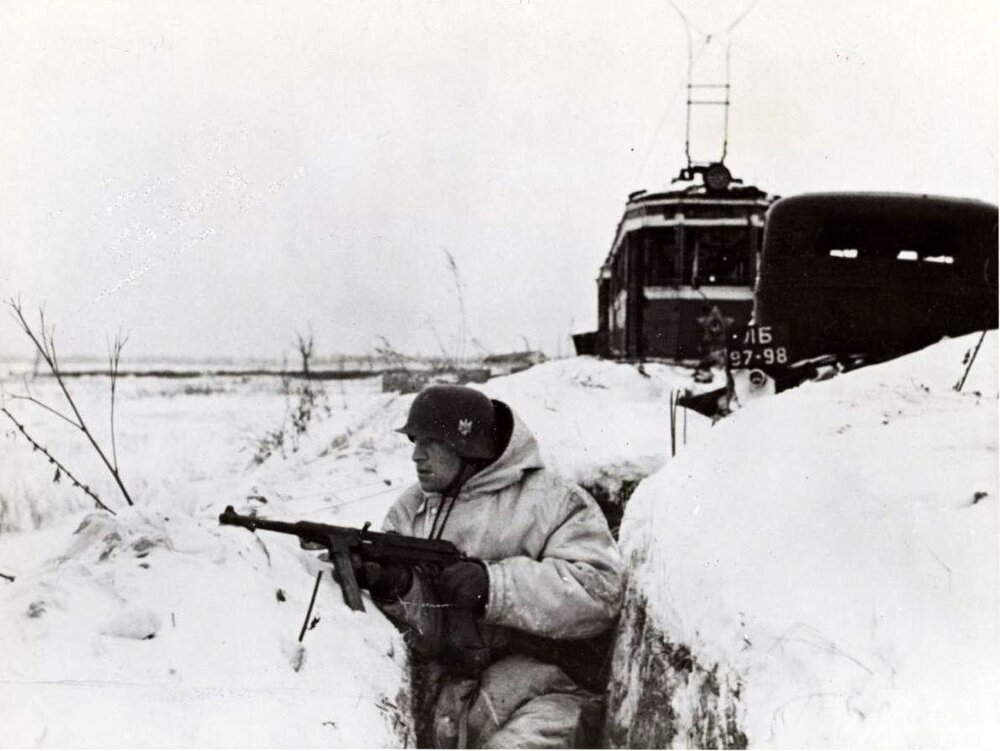 Propagační snímek německé armády zachycující příslušníka Wehrmachtu v zákopu u Leningradu. V pozadí je vidět jednu z leningradských tramvají, která zůstala na území, nad nímž německá vojska získala moc. (zdroj: http://www.gahetna.nl)
