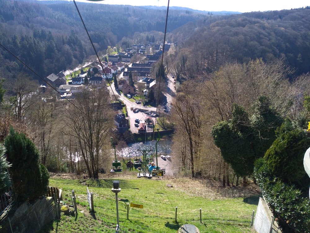 Nebo je libo lanovku? Jedná se o privátní dráhu z roku 1952 o délce zhruba půl kilometru, která vede na místní hrad z městské části Unterburg (na snímku se jedná o ony obytné domy) a překračuje řeku Wupper. Na snímku vyčnívající cesta napravo od Unterburgu (viditelná vpravo od pravého lana) vede ze Solingenu do Unterburgu a dále do Burgu. Trolejbusová točna se nachází od dolní stanice lanovky jen asi 300 m vpravo (na snímku zcela vpravo, tam, kde je les nejtemnější, obec Burg je pak ještě více vpravo a spíše směrem dolů, viz mapu níže).