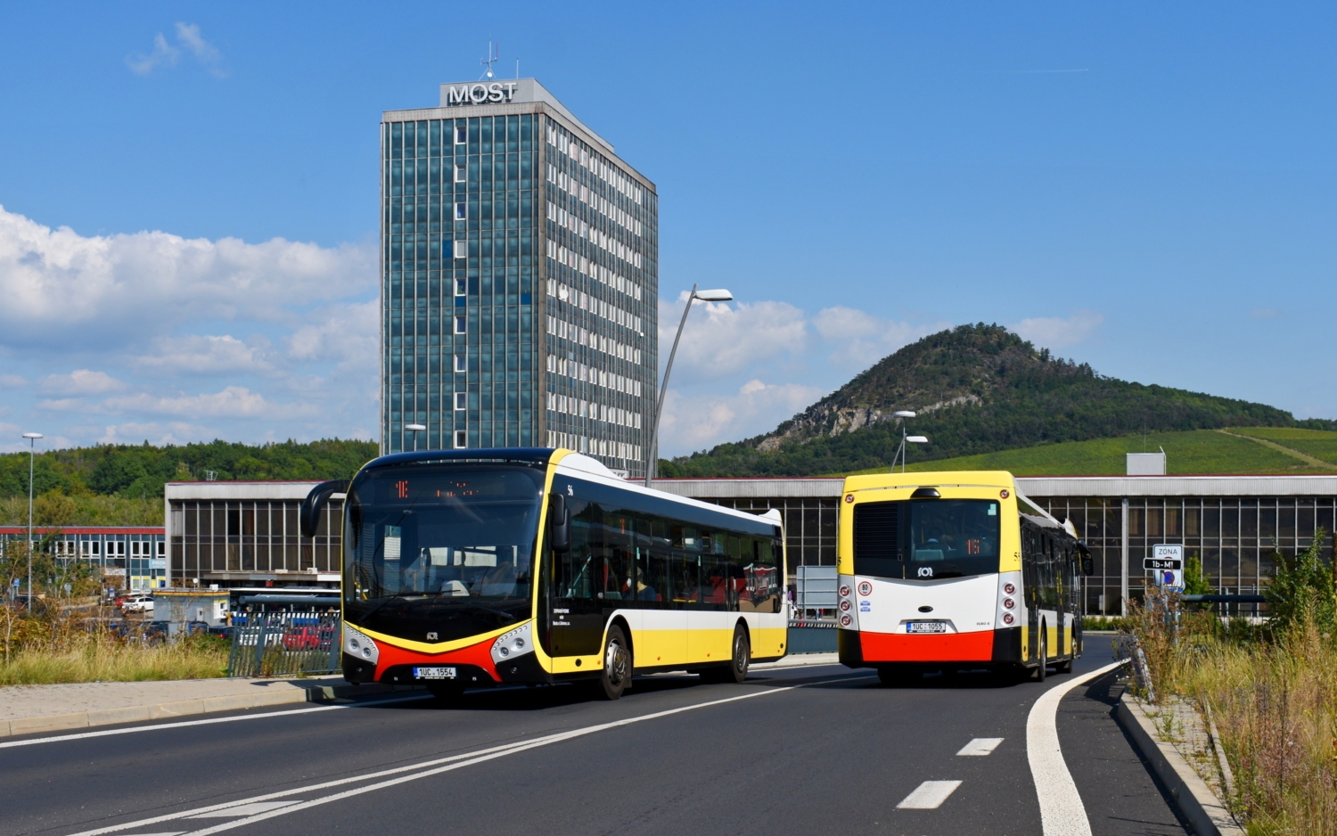 Postupka autobusů SOR NS 12 diesel ev. č. 55 a 56 se setkala 2. září 2021 u mosteckého nádraží. V pozadí se nad nimi tyčí vrch Špičák o výšce 399 m n. m. (foto: Matěj Stach)