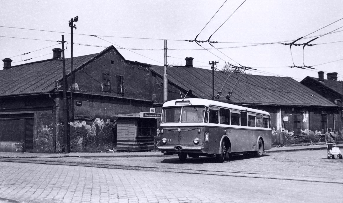 Ostravské trolejbusy měly postupně nahrazovat úzkorozchodné tramvaje ve vybraných relacích, když byl ale v roce 1952 zahájen provoz trolejbusů v Ostravě do Hrušova, o náhradu úzkorozchodek se ještě nejednalo. Trať, jež se stala záhy velmi úspěšná z pohledu počtu přepravených cestujících, neměla původně vůbec v podobě, v níž nakonec vznikla, existovat a sloužit cestujícím. Úlohou trolejbusů mělo být výhledově především napojit nedaleký Důl Stalin II (později Důl Heřmanice). Jenomže stavba v plánované relaci se uskutečnila až v roce 1995, tedy v době, kdy byl už důl zavřený. Postupné nahrazování úzkokolejné dráhy mezi Ostravou a Bohumínem začalo až v roce 1970 (původní tramvajová trať ale byla zkracována už od 60. let v souvislosti s výstavbou nové Bohumínské ulice), trolejbusy ale dorazily jen na okraj Hrušova. K prodloužení směrem do Vrbice či Bohumína nikdy nedošlo a v roce 2003 byla zrušena i smyčka trolejbusů v Hrušově. Na snímku vidíme trolejbus Škoda 8 Tr ev. č. 37 v Hrušově na Žižkově ulici. Trolejbus byl vyřazen v roce 1976 v důsledku vážného poškození po výbuchu plynu pod mostem Pionýrů, po kterém právě projížděl. (sbírka: Libor Hinčica)